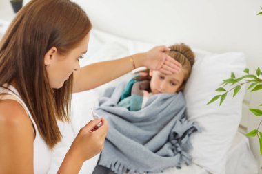 Endişeli genç annenin portresi, küçük hasta çocuğunun termometresiyle evde soğuk algınlığı ya da gripten yatarken kendini kötü hissetmesi. Sağlık hizmetleri kavramı.