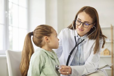 Çocuk doktoru çocuk hastasını muayene ediyor. Genç bayan doktor küçük kızların göğsüne steteskop takıyor ve pediatri kliniğindeki randevusu sırasında ciğerlerini kontrol ediyor. Tıbbi kontrol kavramı