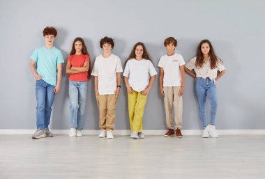 Neşeli çocuklar, öğrenciler ve öğrencilerden oluşan çeşitli ve pozitif bir takımın grup portresi gri bir arkaplanda bir arada duruyor. Mutlular ve birlikteler. Arkadaşlık ve takım çalışması gösteriyorlar..