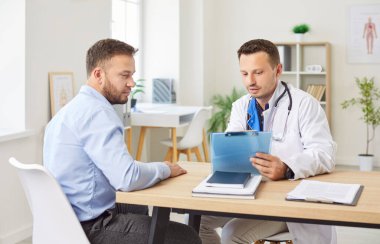 Beyaz üniformalı ciddi bir doktor hastaya danışmanlık yapıyor, pratisyen hekimlik yapıyor, hastaya danışmanlık yapıyor, hastalıkları hastanede, sağlık hizmetlerinde, reçeteli ilaç tedavisinde ve bakımda tartışıyor.