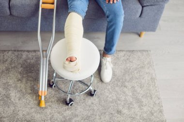 Evdeki oturma odasındaki kanepede oturan kırık, bandajlı bir adamın yakın çekimi. Tıbbi rehabilitasyon ve tedavi görüyor. Kazadan sonra travma ve yaralanma tedavisi görüyor..