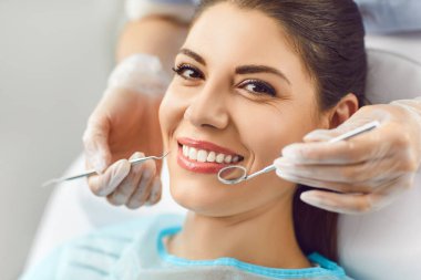 Sağlık kontrolü sırasında dişçi kliniğinde kameraya gülümseyen mutlu kadının portresi. Dişçi muayenehanesinde dişlerini tedavi eden kadın hastaya yakın çekim. Diş bakımı konsepti.