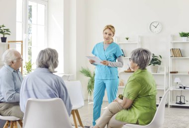 Kıdemli grup sohbetleri, yaşlı hastalar ve üniformalı genç kadın sağlık görevlisi elinde bilgi, müşteriler sağlık şikayetleri hakkında bilgi paylaşımı, bakım destek toplantıları