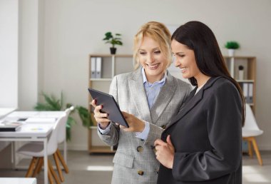 İki iş kadını birlikte çalışıyor, tablet üzerinde çalışıyorlar, proje üzerinde çalışıyorlar, resmi giyiniyorlar, kabinede duruyorlar, bir şeyler tartışıyorlar. Modern teknolojileri kullanan kadın meslektaşlar