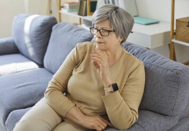 Yaşlı, düşünceli, gözlüklü, rahat kıyafetler giyen, koltukta oturan, hayatı düşünen, evinde rahat hisseden bir kadın. Yaşlılar ve yaşam tarzı konsepti