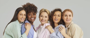 Stüdyonun gri arka planında kameraya bakıp gülümseyen neşeli ve çeşitli kadın arkadaşlarının yakın plan portresi. Çeşitlilik, destek ve takım konsepti. Pankart.