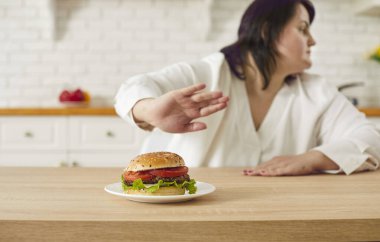 Kes şunu! Artık yağlı yemek istemiyorum. Şişman kadın diyete başlıyor, kötü alışkanlıkları bırakıyor ve hamburgerlere hayır diyor. Tombul kadın reddediyor ve mutfak masasında nefis et burgeriyle tabağı itiyor.