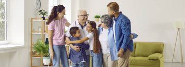 Aile toplantısı. Mutlu çok nesilli aile, evde buluşurken birbirlerini kucakladıkları için mutlular. Yetişkin çocuklar ve torunlarla oturma odasında yaşlı çiftler kucaklaşır. Panoramik görünüm.