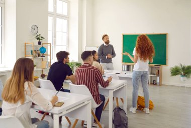 Erkek öğretmen üniversitedeki ders sırasında bayan öğrencinin yanıtını dinler. Liseli kız masasında durur ve öğretmeniyle sohbet eder. Eğitim süreci kavramı.