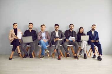 Genç profesyonel iş adamları sırada oturup kameraya bakıyorlar. Bir grup mutlu personel. Görev adayları ellerinde özgeçmişleri olan mülakat daveti bekleyen kişiler.