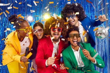 Partide parlak kostümler, kıvırcık peruklar ve renkli büyük bardaklarla mikrofonlara şarkı söyleyen komik bir grup genç, mavi yağmurun arka planında konfeti eşliğinde dans ediyor..