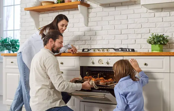 Mutlu aile, genç çift ve çocuk nefis pişmiş lezzetli çöreklerle tepsiyi fırından çıkarıyor, modern mutfakta yemek pişirmeyi seviyor, ev yapımı aile pastaları, aşçılık hobisi, çörekler, lezzetli sıcak tatlılar.