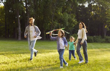 Dışarıda, rüzgarlı bir günde parkta uçurtma uçuran mutlu aile fotoğrafı, dışarıda vakit geçirmek. Anne ve baba çocuklarıyla oynuyor, yazın eğleniyorlar.
