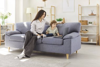 Anne ve küçük çocuk dizüstü bilgisayar kullanarak vakit geçiriyorlar, bebek bakıcısı evdeki koltukta oturuyor, mal alıyor, oyuncak alıyor, film seyrediyor, çizgi film seyrediyor ya da çocuk gelişimi için dinleniyor.