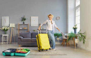 Neşeli bayan turist evde tatil bavullarını toplarken eğleniyor. Sarı çantasıyla dans eden genç bir kadın, mutlu ve heyecanlı bir şekilde seyahat macerasına başlıyor. Yaz tatili bagaj konsepti