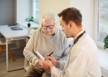 Profesyonel doktor yaşlı hastaya danışmanlık yapıyor, check-up sırasında reçete yazıyor, olgun bir adama sağlık hizmeti tavsiyeleri veriyor. Yaşlılar ve sağlık kavramı. 