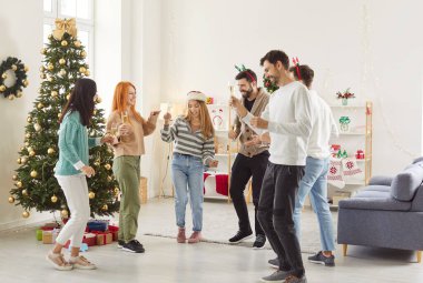 Bir grup genç arkadaş ellerinde şampanya kadehleriyle salonda dans ediyorlar. Mutlu insanlar evde yeni yıl partisini kutluyor. Kutlama ve kış tatili konsepti.