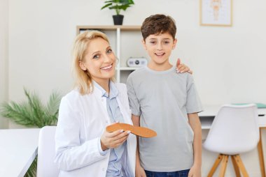 Klinikteki kadın ortopedist sarılan çocuk, yakın plan. Rahat ortopedik taban seçimi. Konsept çocuk doktoru, doktor teşhisi, pediatrik ortopedi, tıbbi rahatlık. 