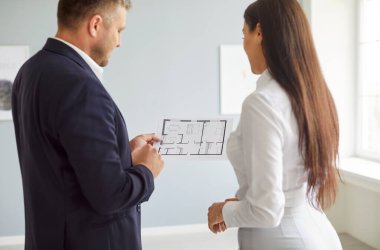 Emlakçı ya da emlakçı yeni bir ev ya da ofisin planını müşterisiyle tartışır. Proje incelemesinde bir mülk alımı ve sergilenen takım çalışması için planlama safhası vurgulanıyor.