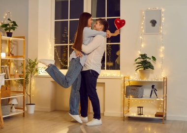 Sevgililer Günü. Elinde kırmızı folyo balonu tutan genç ve mutlu bir kadın tatilde erkek arkadaşına sarılıyor ve onu tebrik ediyor. Gülümseyen bir çift, aşık bir erkek ve bir kadın, evde durmuş birbirlerine bakıyorlar..