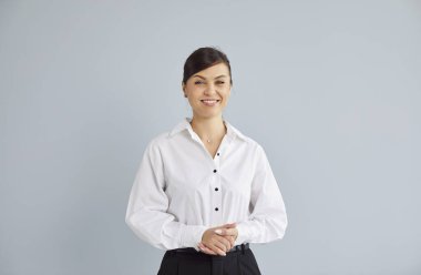 Mutlu gülümseyen genç iş kadınının portresi gri stüdyo arka planında izole edilmiş ve kameraya neşeli görünüyor. Zeki, neşeli, resmi kıyafetler giyen, fotokopi odasıyla evde duran bir kız..