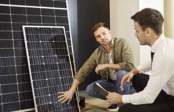 Dükkan asistanı, müşteriye güneş paneli seçmesinde yardım ediyor. Mağazadaki satıcı, gelecekteki ekonomi için yatırım yapmak isteyen genç bir erkek müşteriye fotovoltaik panellerin teknolojik avantajlarından bahsediyor.