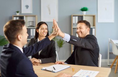Pozitif müşteriler ve danışman, tamamlanmış bir anlaşmayı sembolize ederek ofis toplantısında başarılı bir beşlik çakışmasını kutluyorlar. İş sözleşmesi başarısı ve takım çalışması.
