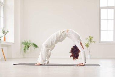 Kadın spor salonunda yoga yapıyor, esneme egzersizi yapıyor ya da spor yaparken briç pozisyonu alıyor. Dayanıklılık, esneklik ve denge gösteriyor, genel uygunluğu arttırıyor..