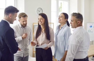 Ofis çalışanları bir grup toplantısı düzenliyor, gülüyor ve iletişim kuruyorlar. Bu iş ortamı, hedeflere ulaşmak için takım çalışmasını, bağlantıyı ve etkili işbirliğini teşvik etmektedir..