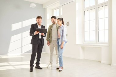 Yetişkin, kendine güvenen profesyonel bir emlakçının portresi modern yeni apartman dairesinde birkaç müşteriyle birlikte emlak satın alma sözleşmesini tartışıyor. Taşınma, kira ve emlak piyasası kavramı.