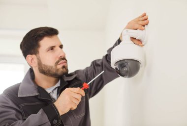 Üniformalı genç bir teknisyenin portresi. Kapıya güvenlik kamerası yerleştiriyor. Modern ofiste ya da evde güvenlik kameralarını tamir ederken erkek işçi tornavida kullanıyor.