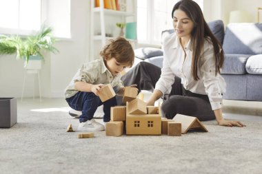 Genç ve mutlu anne, evdeki oturma odasında küçük sevimli çocukla eğitici tahta oyuncaklarla oynuyor. Bayan ebeveyn oğluyla vakit geçiriyor. Aile eğlencesi ve insan konsepti.
