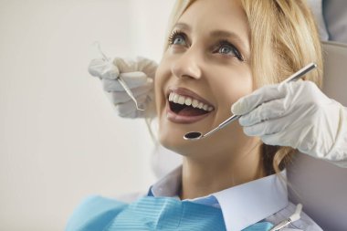 Kadın hasta dişçi randevusuna klinikte katılıyor, doktor ağız bakımını kontrol ediyor, diş aletlerini kullanıyor, profesyonel bir arka planda diş hekimliğine odaklanıyor ve sağlık kontrolünde detaylara dikkat ediyor..