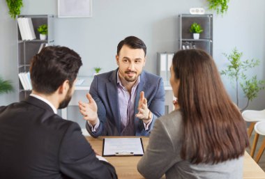 Genç, beyaz bir çift masada oturmuş sözleşmeyi tartışıyor ve emlakçı ya da mali danışman ile görüşüyorlar. Sigortacı kadın ve erkeğe danışmanlık yapıyor..