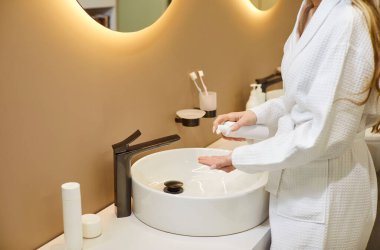 Aynanın yanında duran, bornoz giyen, losyon süren, banyo, banyo, güzellik, cilt bakımı, krem sürme, güzellik hijyeni rutini