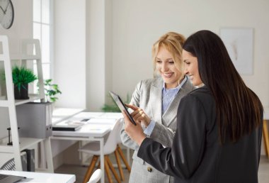 Genç neşeli bayan iş adamlarının portresi işyerinde duruyor, tablet monitör ekranına bakıyor ve iş projesini ya da şirket finansmanını tartışıyor. Ofiste çalışan iki kadın..