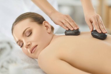 Sıcak taş sırt masajı, spa ve güzellik salonu kadın kozmetik uzmanı, güzellik uzmanı gergin kasları rahatlatıyor, acıyı azaltıyor, sakinleşiyor, zevk alıyor, gençleştiriyor, gevşiyor, tedavi oluyor, kadın sağlığını geliştiriyor.