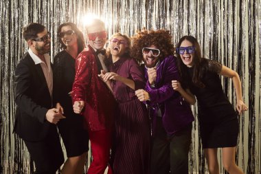 Parlak takım elbiseli mutlu gençlerin portresi disko partisinin keyfini çıkarıyor ve gümüş folyo folyo arka planda eğleniyorlar. Gece kulübündeki dansçılar. Kutlama konsepti.