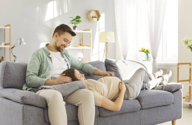 Oturma odasındaki kanepede oturan genç adam hamile karısı karnına dokunurken konuşuyor. Bebek bekleyen mutlu çift ebeveyn olmaya hazırlanıyor. Hamilelik ve ebeveynlik kavramı.