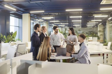Bir grup iş arkadaşı ya da iş adamı bir ofiste birlikte çalışıyor, sohbet ediyor ve takım toplantısı sırasında belgeleri gözden geçiriyorlar. İletişim, takım çalışması ve profesyonel müdahale..