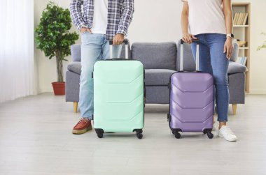 Tatil gezisine hazır bir çift. Evde bavulları paketlenmiş iki kişi. Oturma odasında elinde nane ve mor bavullarla duran bir adam ve kadın. İnsan bacakları, düşük kesim çekim. Tatil seyahati kavramı