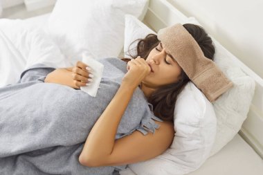 Yatakta yatan hasta genç kadın ekoseyle kaplı soğuk, mevsimsel enfeksiyon ya da evde grip virüsü yüzünden acı çekiyor. Kafasında ıslak havluyla öksüren, elinde kağıt peçeteler tutan sağlıksız bir kız..