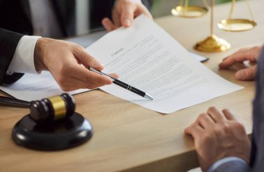 Legal advisor helping client to sign contract, showing with pen place for signature, giving consultation in his cabinet. Unrecognizable man making agreement with lawyer. Legal law concept