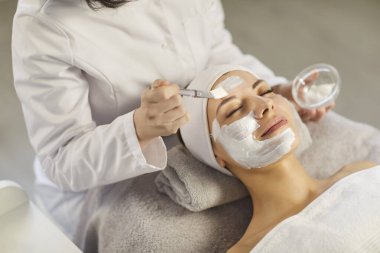 Dermatolog, kozmetolog güzellik uzmanı kadın yüzüne fırça sürerek nazikçe cilt kremi maskesi uyguluyor nemlendirici, spa salonunda veya klinikte profesyonel hijyenik rahatlama seansı, güzellik tedavisi.