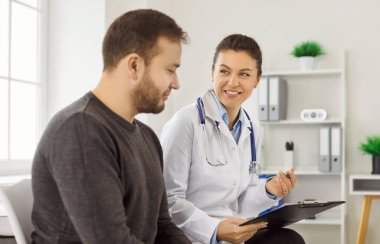 Dost canlısı doktor ve hasta klinikteki tıbbi muayene sırasında tedavi planını tartıştılar. Kadın tıp çalışanı, tıbbi danışma sırasında panoyu tutuyor ve adama gülümsüyor. Tıp konsepti.