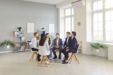 Muhtelif ve mutlu meslektaşlar bir ofis toplantısı sırasında bir çember içinde oturuyorlar. Ekip etkili iletişim yoluyla çalışır, konuşur ve profesyonel takım çalışmasını teşvik eder..