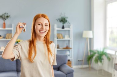 Elinde anahtarlarla kameraya bakan, gülümseyen kızıl saçlı güzel bir kadının portresi. Mutlu, yeni ev sahibi, gayrimenkul satın almanın keyfini çıkarıyor..