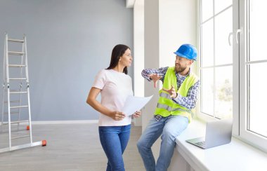 Genç kadın ev sahibi, yeni dairenin tasarımı ya da onarımı hakkında konuşuyor. Ustabaşı boş odada duruyor. İnşaatçıyla iç dekorasyon ya da ev düzeni hakkında görüşeceğim. Taşınma konsepti.