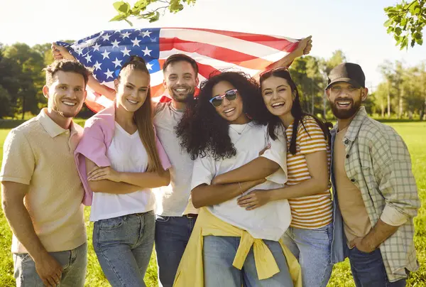 Mutlu, çeşitli gülümseyen genç insanlar. Ellerinde bayrak, günlük giysiler içinde dışarıdaki yaz parkında birlikte duran kameraya bakıyorlar. Bağımsızlık Günü ve vatanseverlik kavramı.
