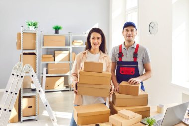 Teslimat servisinden mutlu gülümseyen adam portresi depoda ya da karton kutularla dolu dağıtım merkezinde kadın küçük iş sahibiyle birlikte nakliye işi yapıyor.